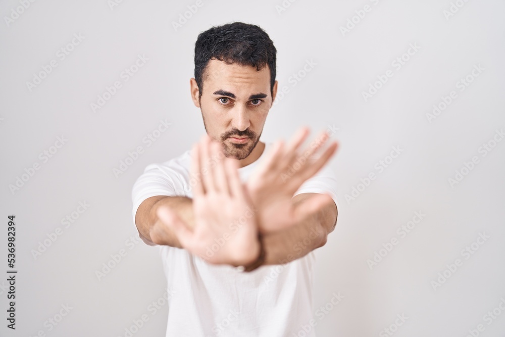 Handsome hispanic man standing over white background rejection expression crossing arms and palms doing negative sign, angry face