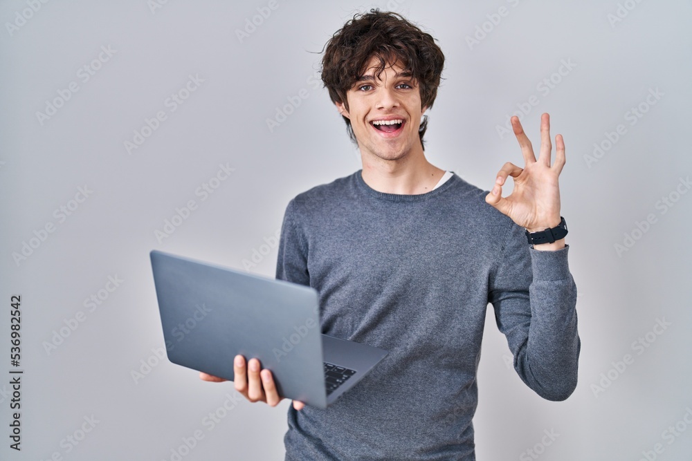 Young man working using computer laptop doing ok sign with fingers, smiling friendly gesturing excellent symbol Young man working using computer laptop doing ok sign with fingers, smiling friendly gesturing excellent symbol