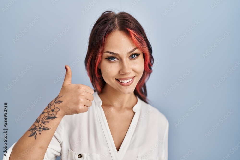Young caucasian woman wearing casual white shirt over isolated background doing happy thumbs up gesture with hand. approving expression looking at the camera showing success. Young caucasian woman wearing casual white shirt over isolated background doing happy thumbs up gesture with hand. approving expression looking at the camera showing success.