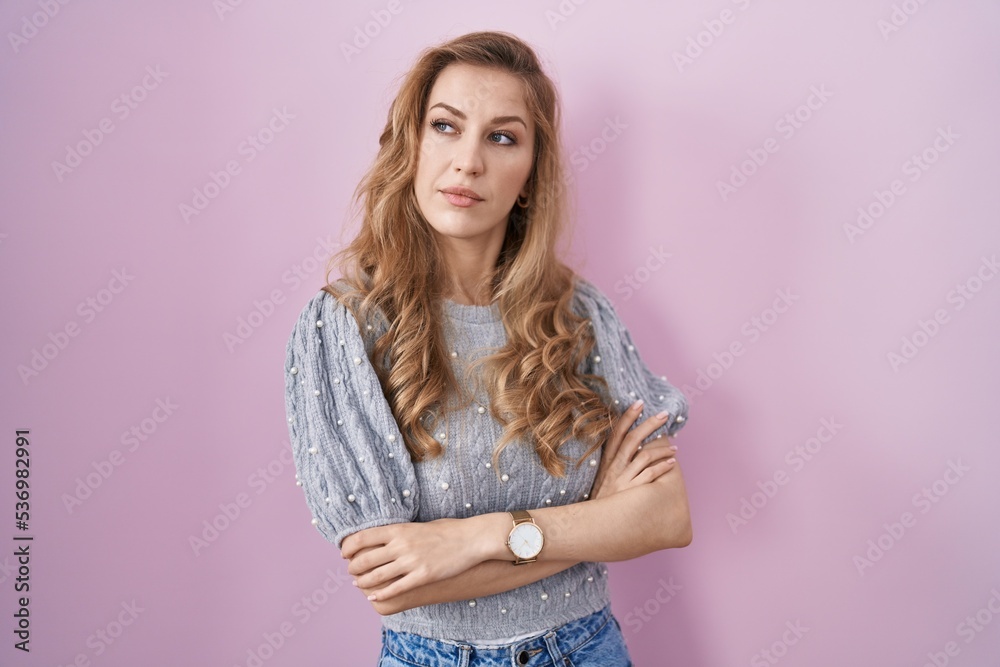 Beautiful blonde woman standing over pink background looking to the side with arms crossed convinced and confident Beautiful blonde woman standing over pink background looking to the side with arms crossed convinced and confident