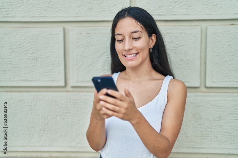 Young beautiful hispanic woman smiling confident using smartphone over isolated white brick background