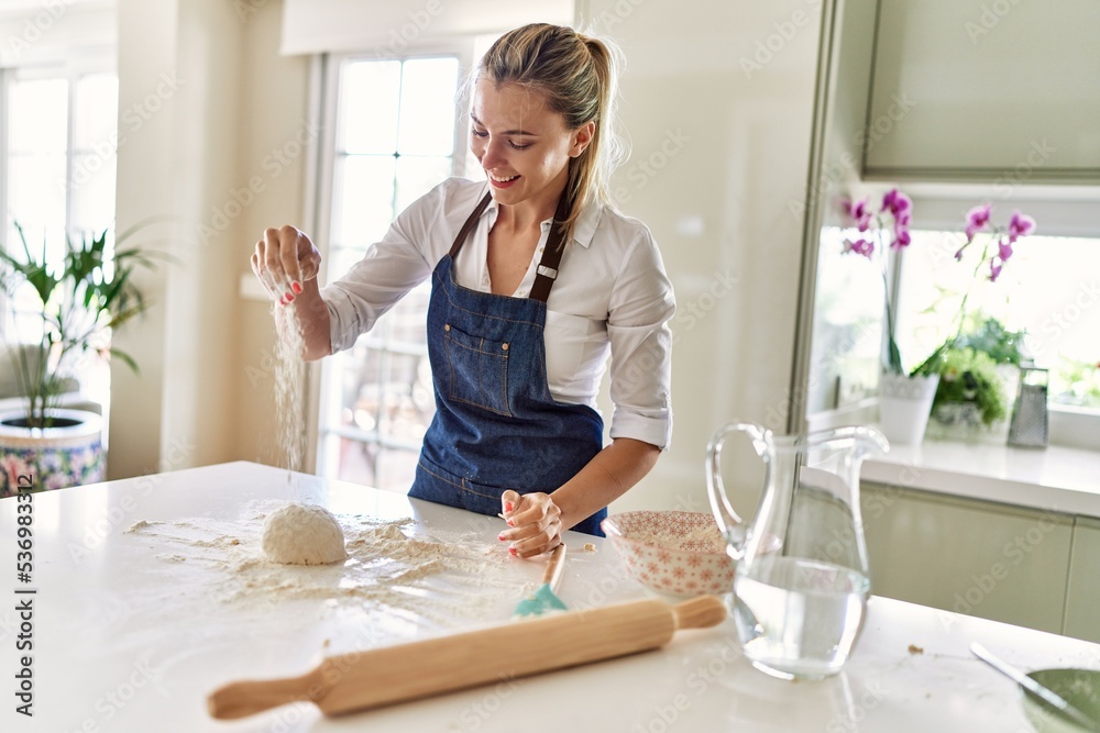 Young blonde woman smiling confident make pizza dough with hands at kitchen