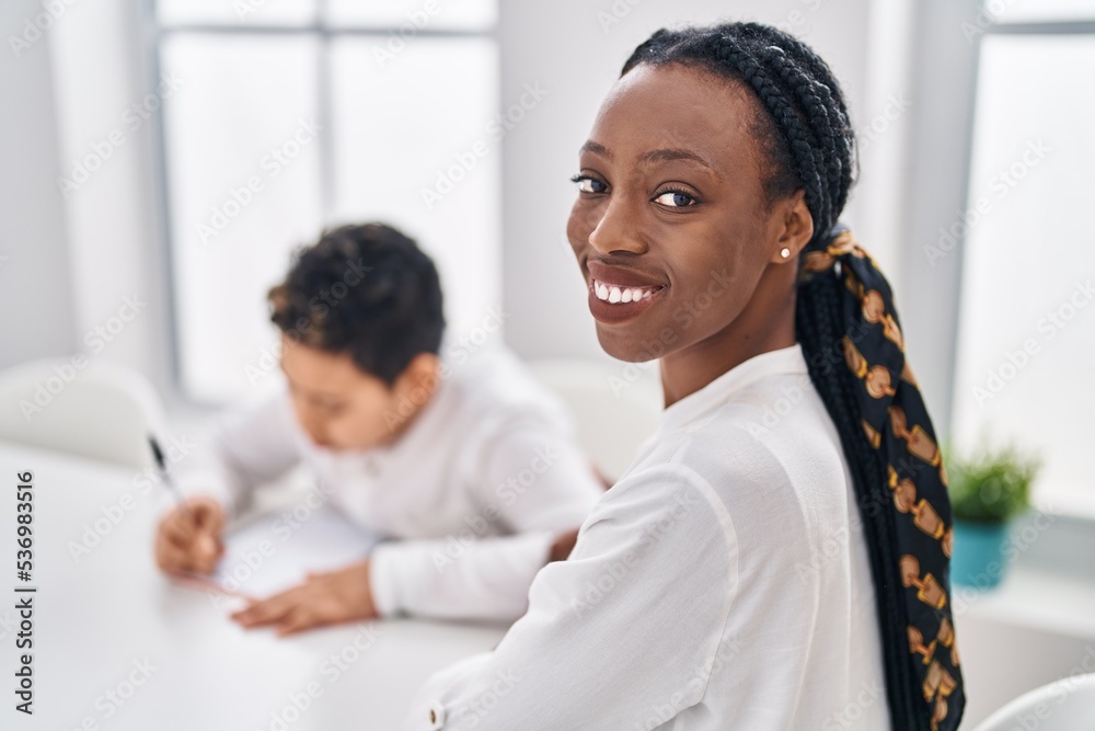 African american mother and son writing on notebook sitting on table at home African american mother and son writing on notebook sitting on table at home