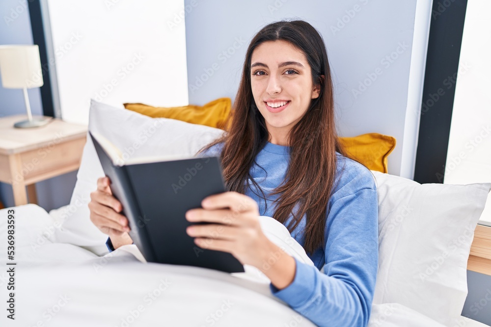 Young beautiful hispanic woman reading book sitting on bed at bedroom Young beautiful hispanic woman reading book sitting on bed at bedroom
