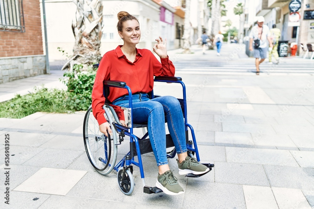 Young brunette woman sitting on wheelchair outdoors doing ok sign with fingers, smiling friendly gesturing excellent symbol Young brunette woman sitting on wheelchair outdoors doing ok sign with fingers, smiling friendly gesturing excellent symbol