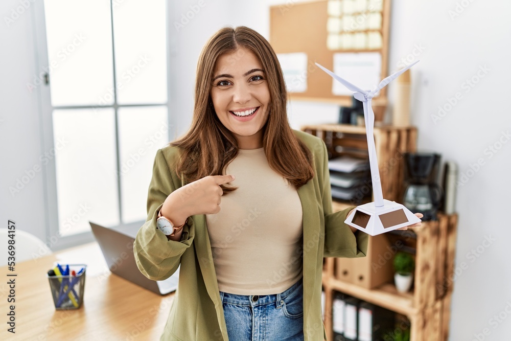 Young brunette woman holding solar windmill for renewable electricity at the office pointing finger to one self smiling happy and proud Young brunette woman holding solar windmill for renewable electricity at the office pointing finger to one self smiling happy and proud