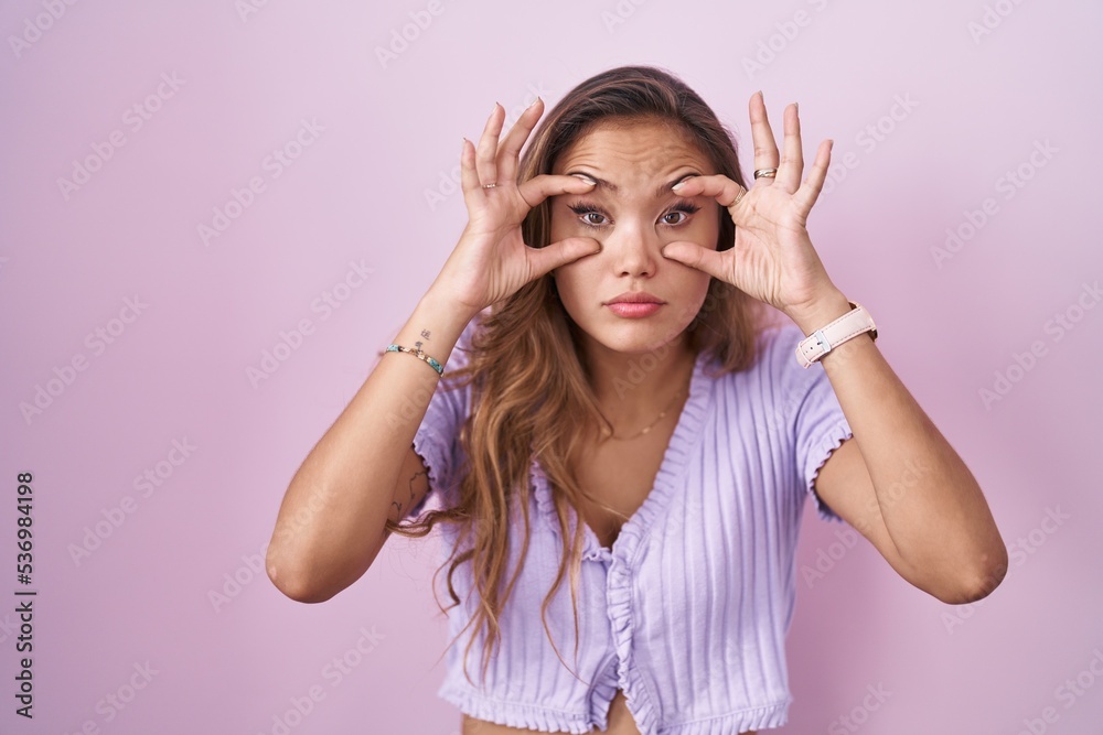 Young hispanic woman standing over pink background trying to open eyes with fingers, sleepy and tired for morning fatigue Young hispanic woman standing over pink background trying to open eyes with fingers, sleepy and tired for morning fatigue