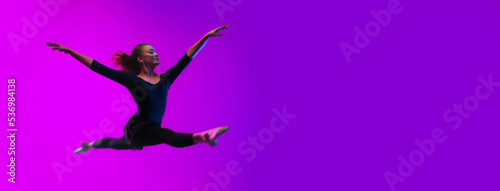 Modern dance girl dancer jumping up dancing in neon light doing gymnastic exercises in studio, wide banner, copy space. © Halfpoint