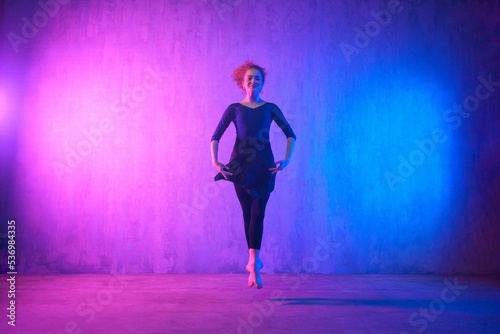 Modern dance girl dancer dancing in neon light doing gymnastic exercises in studio  copy space.
