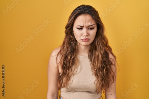 Young hispanic woman standing over yellow background skeptic and nervous, frowning upset because of problem. negative person.