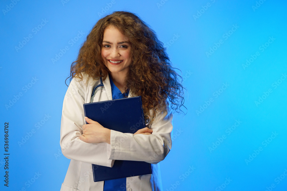 Studio shot of a young female doctor looking at camera against a blue background. Studio shot of a young female doctor looking at camera against a blue background.
