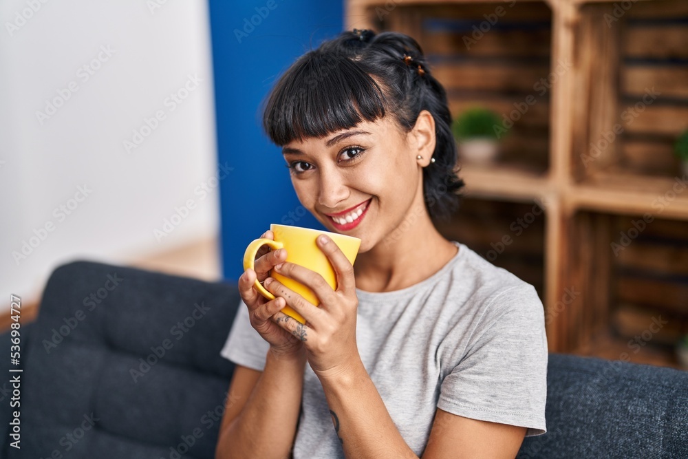 Young woman drinking coffee sitting on sofa at home