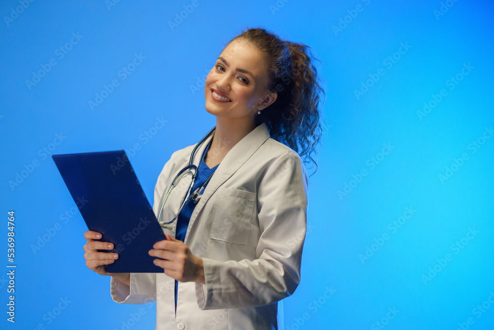 Studio shot of a young female doctor looking at camera against a blue background. Studio shot of a young female doctor looking at camera against a blue background.