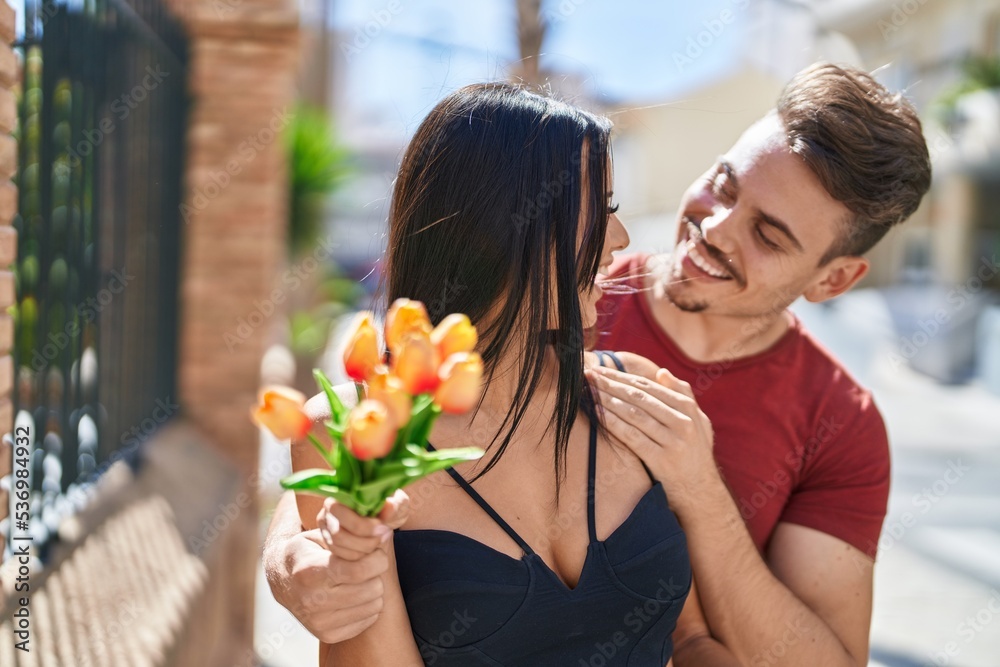 Man and woman couple hugging each other holding bouquet of flowers at street