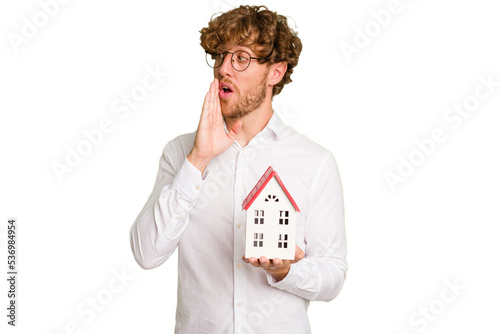 Business caucasian man holding toy house isolated on white background is saying a secret hot braking news and looking aside