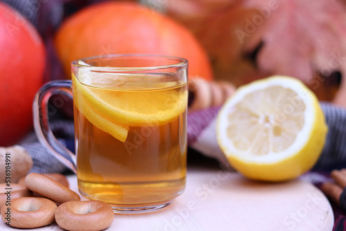 Glass cup with warm tea with lemon close-up on the background of pumpkins. Autumn composition with selective focus.