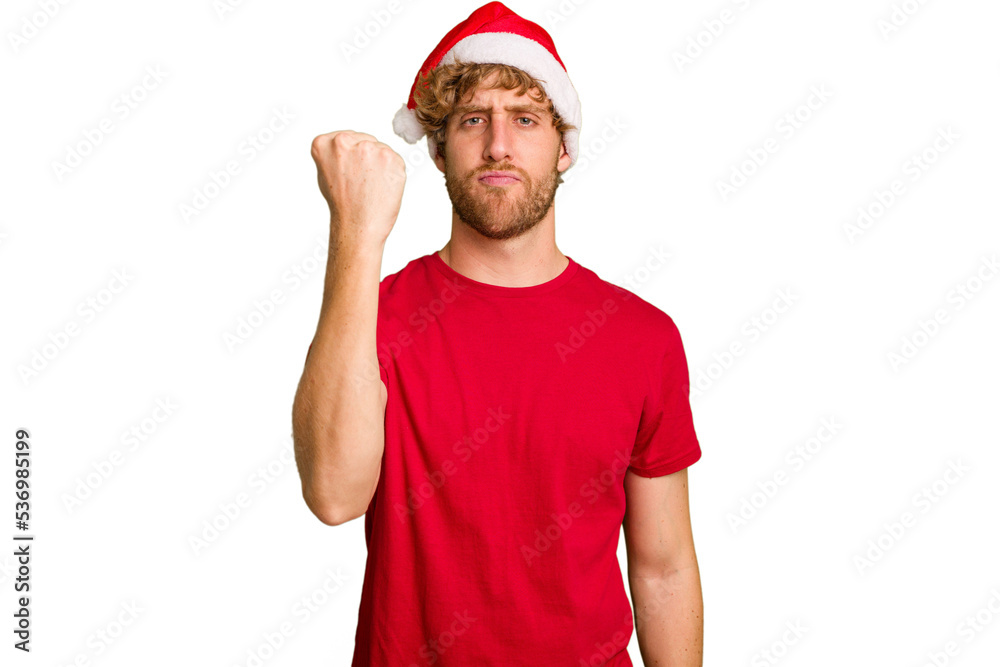 Young caucasian man wearing a Christmas Santa hat isolated on white background showing fist to camera, aggressive facial expression. Young caucasian man wearing a Christmas Santa hat isolated on white background showing fist to camera, aggressive facial expression.