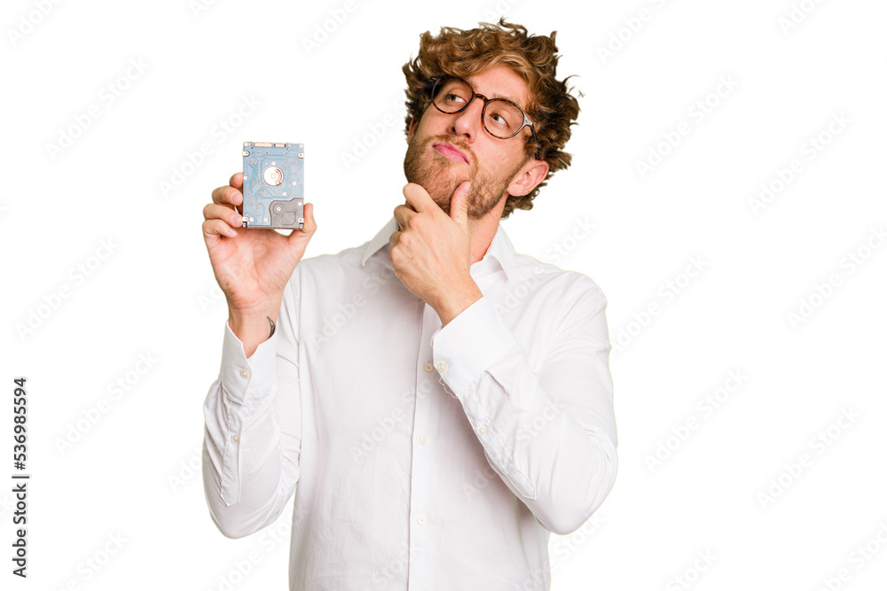 Young caucasian informatic man holding a hard drive isolated on white background looking sideways with doubtful and skeptical expression. Young caucasian informatic man holding a hard drive isolated on white background looking sideways with doubtful and skeptical expression.