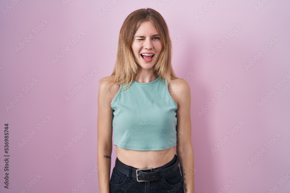 Blonde caucasian woman standing over pink background winking looking at the camera with sexy expression, cheerful and happy face. Blonde caucasian woman standing over pink background winking looking at the camera with sexy expression, cheerful and happy face.