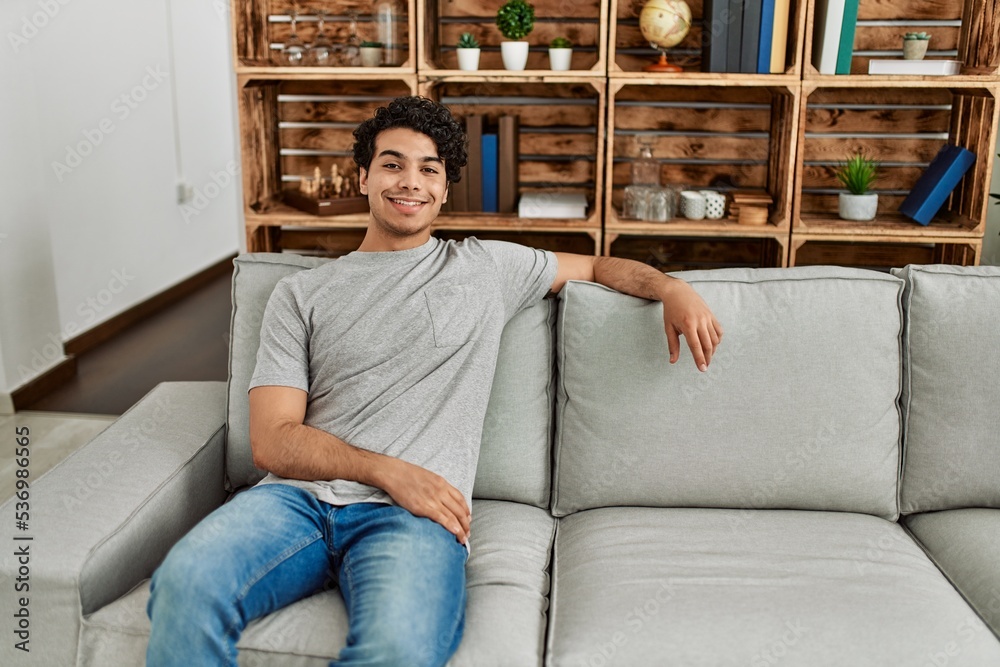 Young hispanic man smiling happy sitting on the sofa at home.
