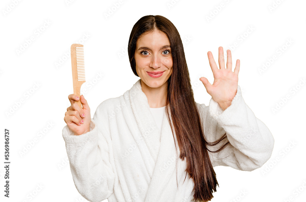 Young caucasian woman holding an hair comb isolated smiling cheerful showing number five with fingers. Young caucasian woman holding an hair comb isolated smiling cheerful showing number five with fingers.