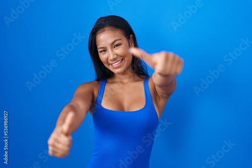 Hispanic woman standing over blue background approving doing positive gesture with hand, thumbs up smiling and happy for success. winner gesture. © Krakenimages.com