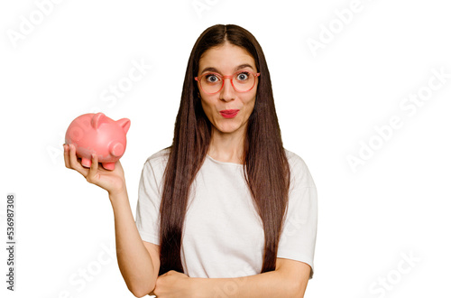 Young caucasian woman holding a piggy bank isolated shrugs shoulders and open eyes confused.