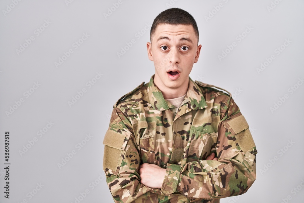 Young man wearing camouflage army uniform afraid and shocked with surprise expression, fear and excited face.