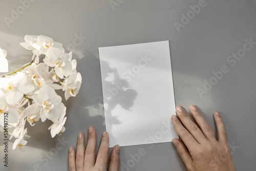 Hands are holding an empty white A5 form on a gray background. Layout top view