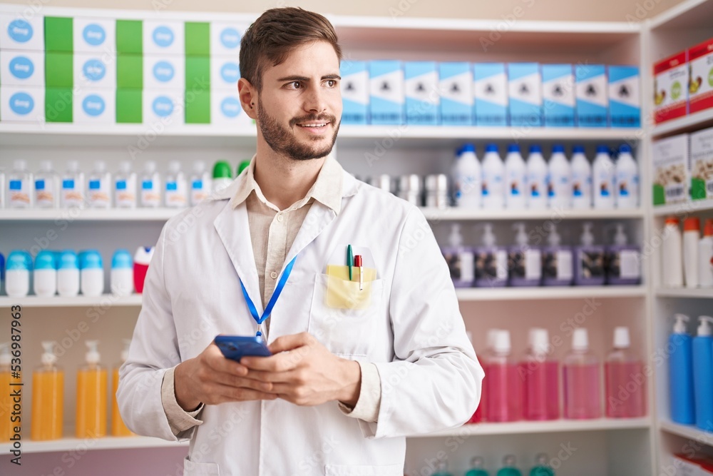 Young caucasian man pharmacist using smartphone working at pharmacy Young caucasian man pharmacist using smartphone working at pharmacy