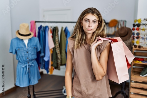 Young blonde woman holding shopping bags at retail shop relaxed with serious expression on face. simple and natural looking at the camera.