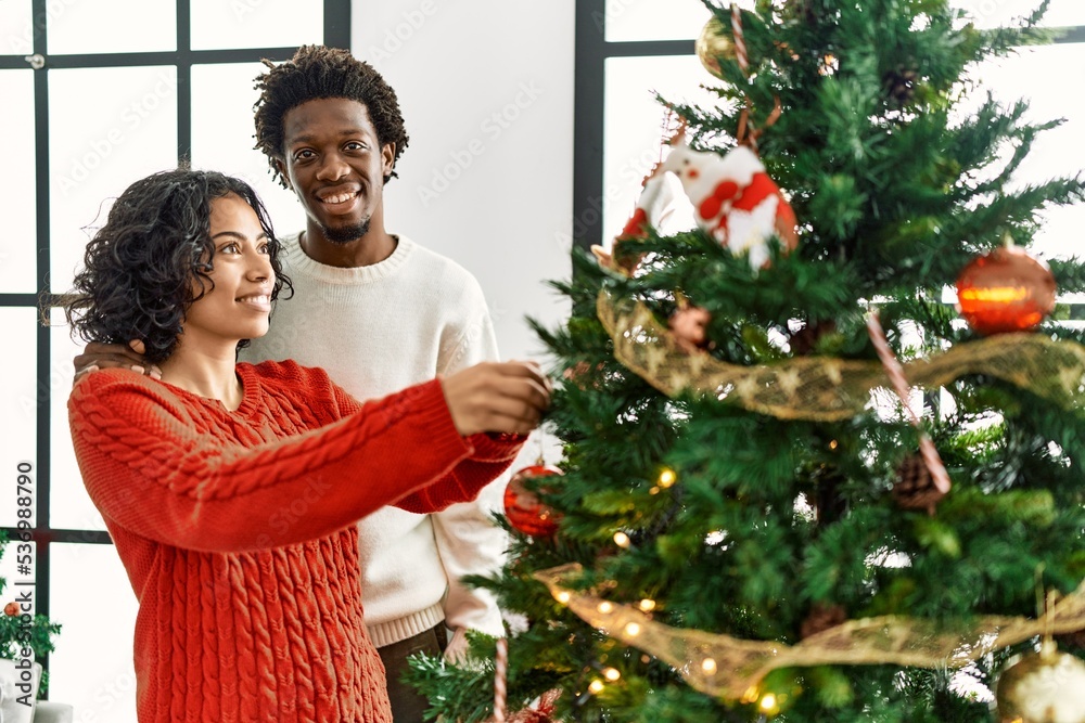 Young interracial couple smiling happy decorating christmas tree at home. Young interracial couple smiling happy decorating christmas tree at home.