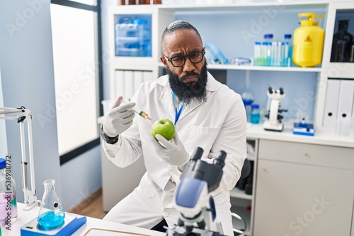 African american man working at scientist laboratory with apple skeptic and nervous, frowning upset because of problem. negative person.