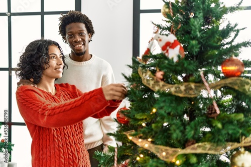 Young interracial couple smiling happy decorating christmas tree at home.