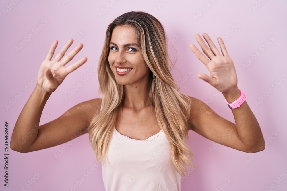 Young blonde woman standing over pink background showing and pointing up with fingers number nine while smiling confident and happy. Young blonde woman standing over pink background showing and pointing up with fingers number nine while smiling confident and happy.