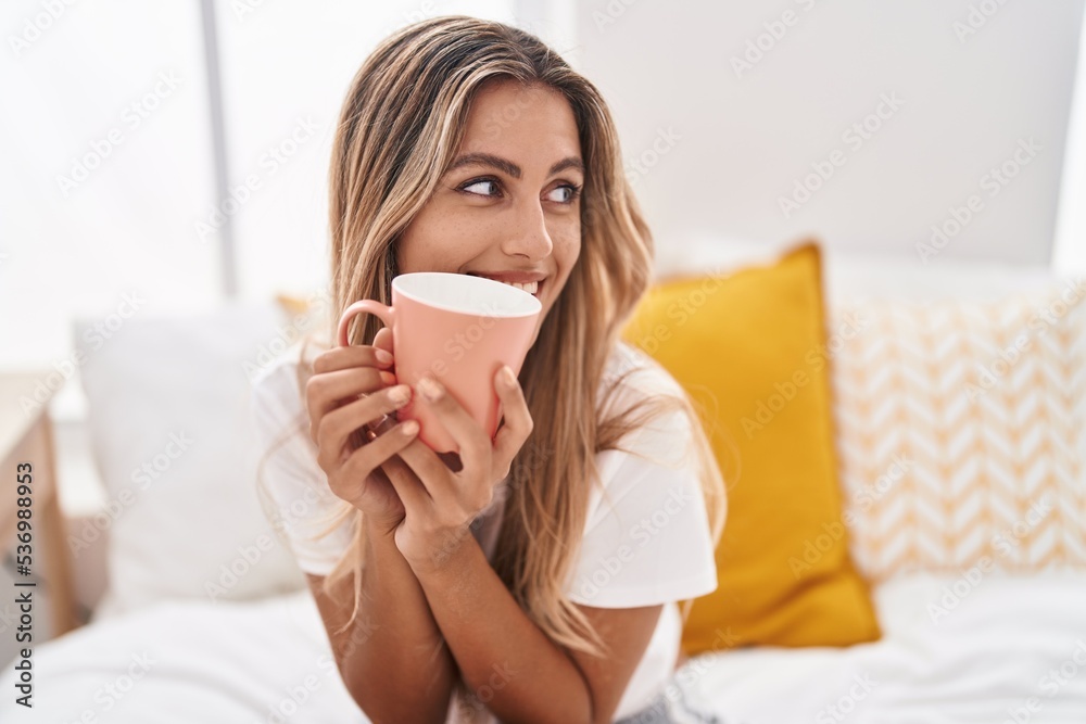 Young blonde woman drinking cup of coffee sitting on bed at bedroom Young blonde woman drinking cup of coffee sitting on bed at bedroom