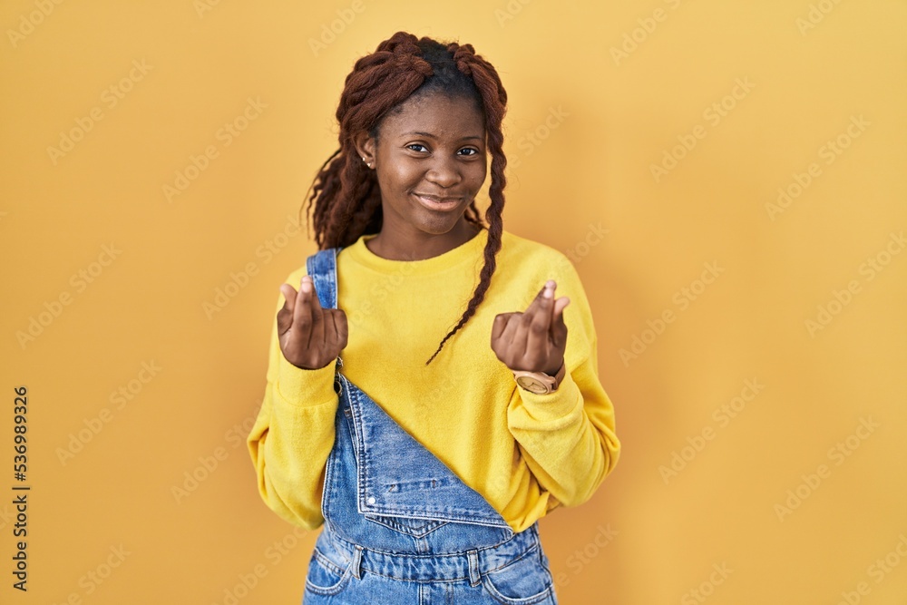 African woman standing over yellow background doing money gesture with hands, asking for salary payment, millionaire business African woman standing over yellow background doing money gesture with hands, asking for salary payment, millionaire business