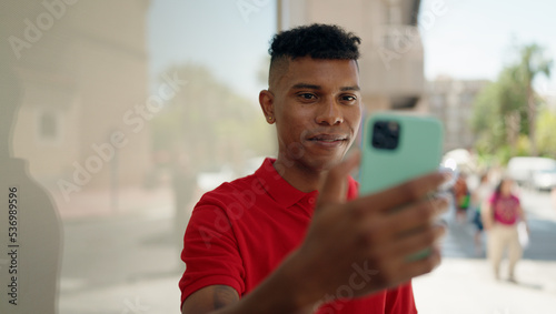 Young latin man smiling confident using smartphone at street