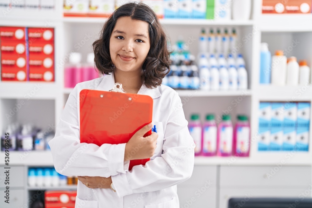 Young woman pharmacist hugging clipboard at pharmacy