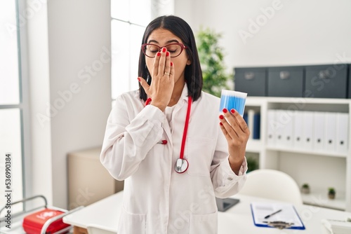 Young hispanic doctor woman holding cotton buds covering mouth with hand  shocked and afraid for mistake. surprised expression