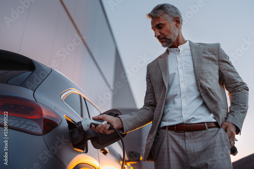 Businessman, holding power supply and charging his electric car during sunset. Concept of ecology tranport. photo
