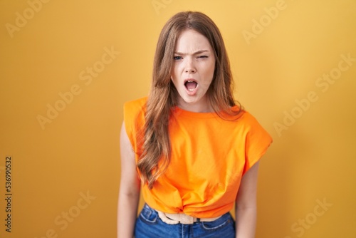 Caucasian woman standing over yellow background angry and mad screaming frustrated and furious, shouting with anger. rage and aggressive concept. © Krakenimages.com