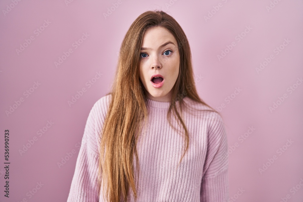 Young caucasian woman standing over pink background in shock face, looking skeptical and sarcastic, surprised with open mouth Young caucasian woman standing over pink background in shock face, looking skeptical and sarcastic, surprised with open mouth