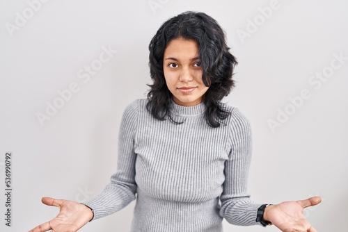 Hispanic woman with dark hair standing over isolated background clueless and confused with open arms, no idea concept.