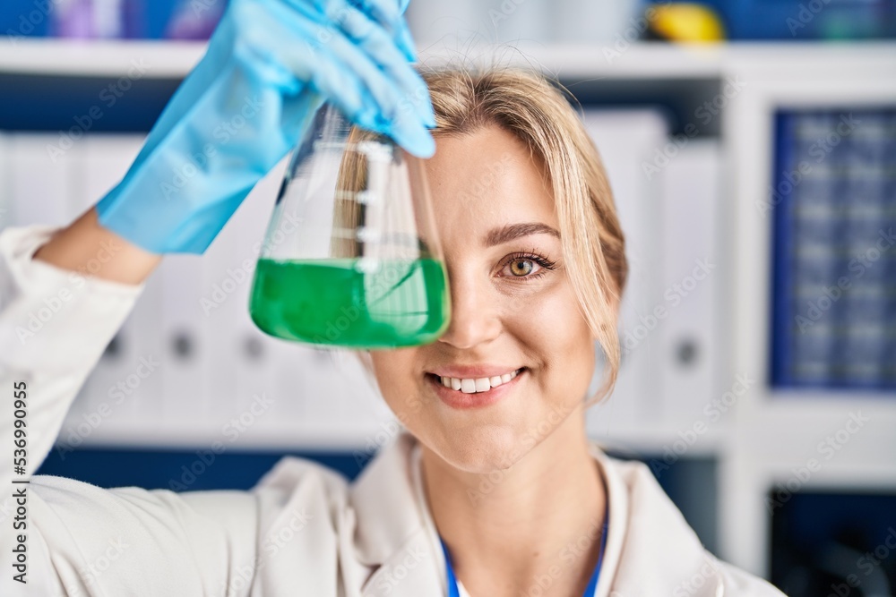 Young blonde woman scientist holding test tube over eye at laboratory Young blonde woman scientist holding test tube over eye at laboratory