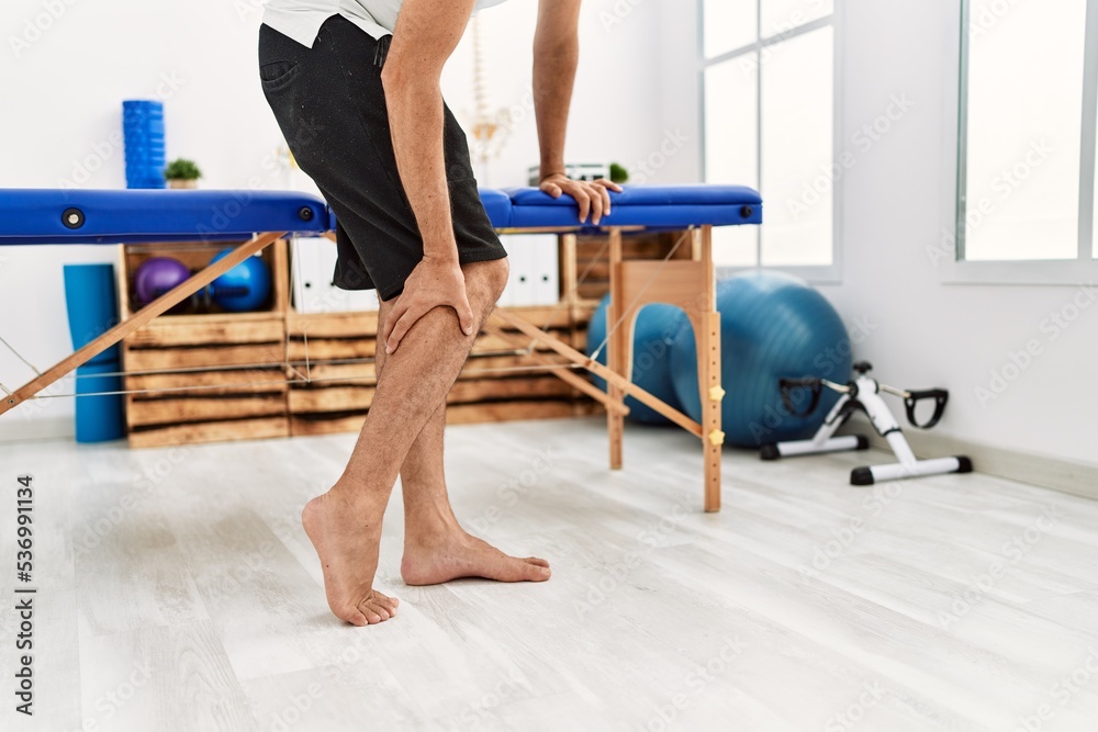 Middle age grey-haired man patient suffering for leg pain standing at rehab clinic Middle age grey-haired man patient suffering for leg pain standing at rehab clinic