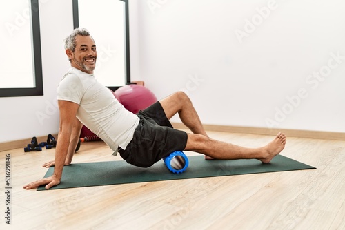 Middle age grey-haired man using foam roller stretching at sport center