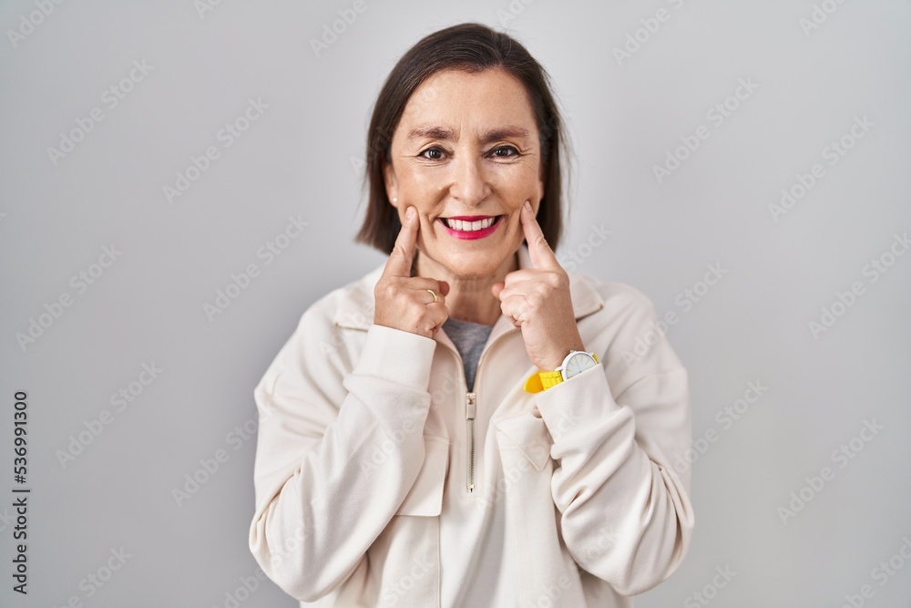 Middle age hispanic woman standing over isolated background smiling with open mouth, fingers pointing and forcing cheerful smile Middle age hispanic woman standing over isolated background smiling with open mouth, fingers pointing and forcing cheerful smile
