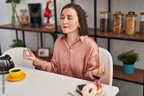 Middle age woman doing yoga exercise sitting on table at home