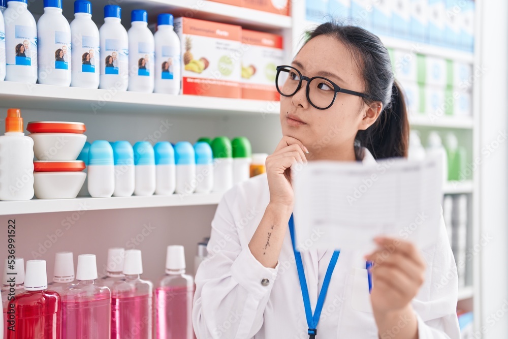 Young chinese woman pharmacist reading prescription at pharmacy